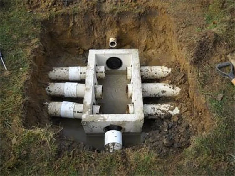 Concrete septic distribution box exposed in an excavation, with outlet pipes running to the field lines